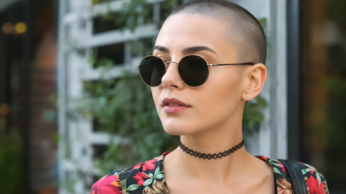 Junge Frau mit Glatze und runder Sonnenbrille