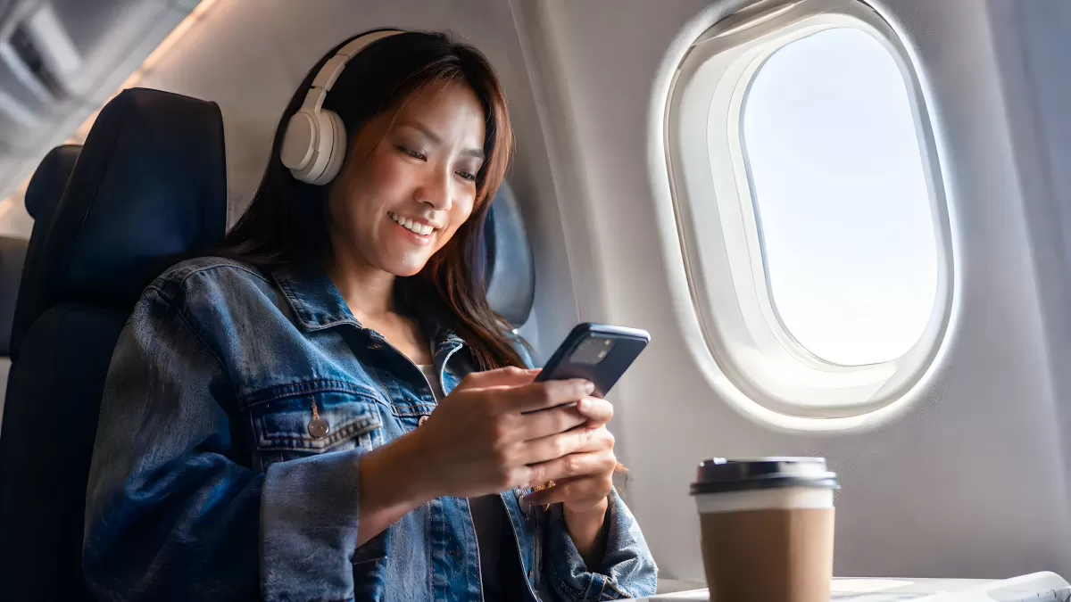 Junge Frau mit Kopfhörern im Flugzeug am Smartphone