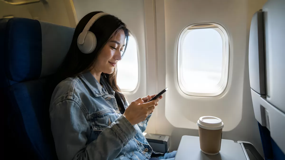 Junge Frau mit Smartphone und Kopfhörern im Flugzeug