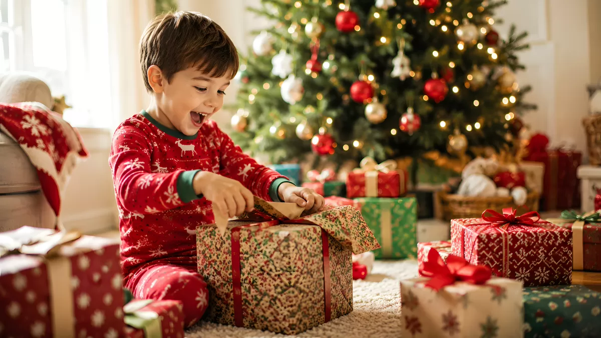 Junge öffnet Weihnachtsgeschenke am geschmückten Tannenbaum