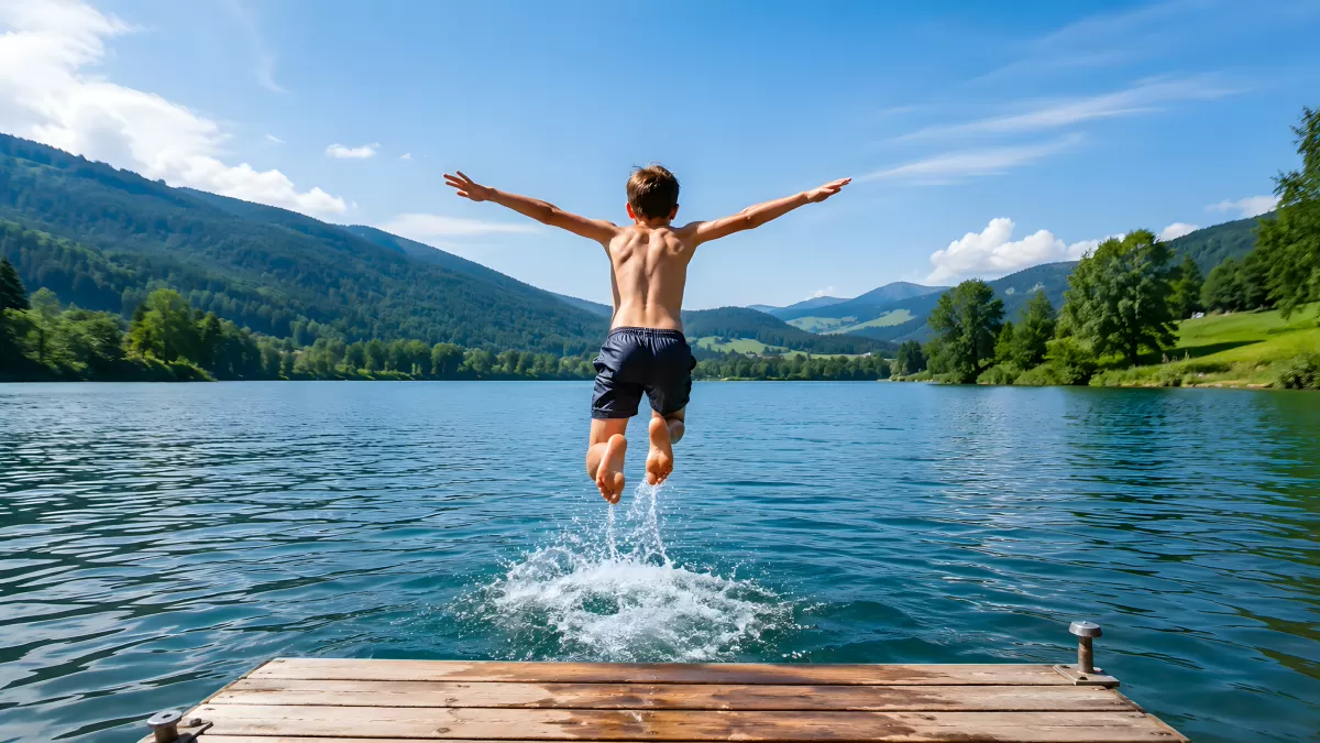 Junge springt vom Holzsteg in einen Bergsee