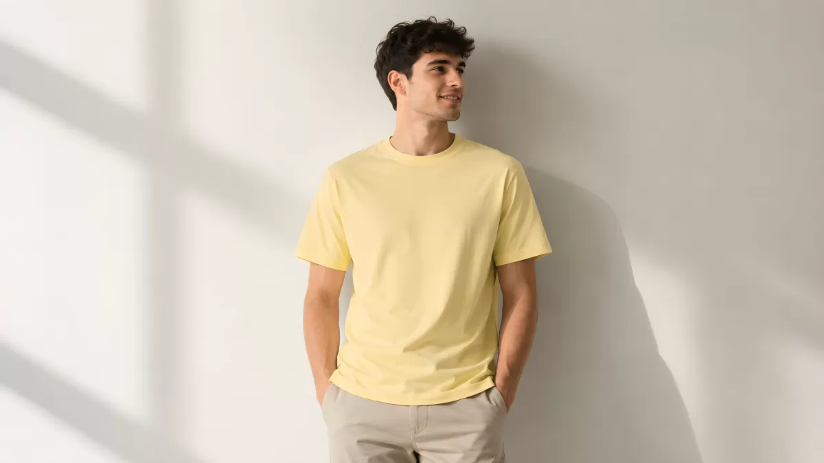 Junger Mann im gelben T-Shirt lehnt an weißer Wand