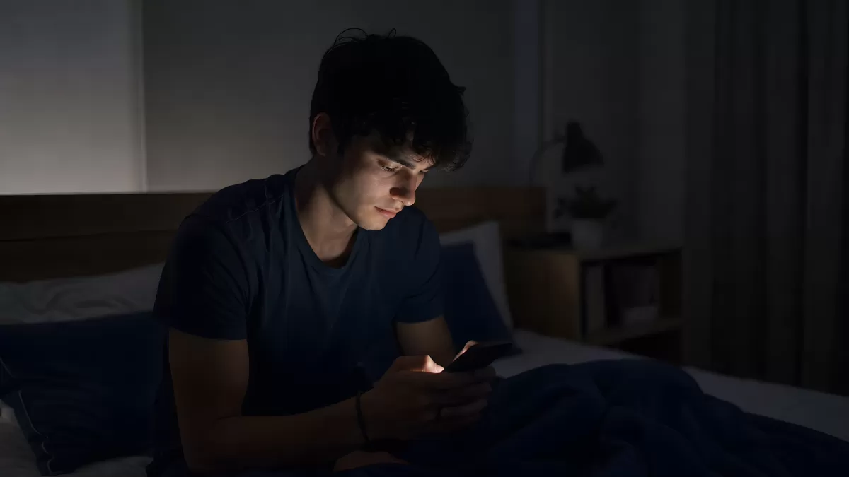 Junger Mann schaut nachts aufs Smartphone im Bett