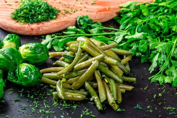 Junger Spargel und Rosenkohl auf dunklem Hintergrund mit frischer Petersilie und Dill