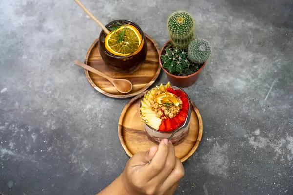 Kaktus und Cold Brew Kaffee mit Orangen neben einem Erdbeer-Apfel Joghurt und Hand mit Löffel