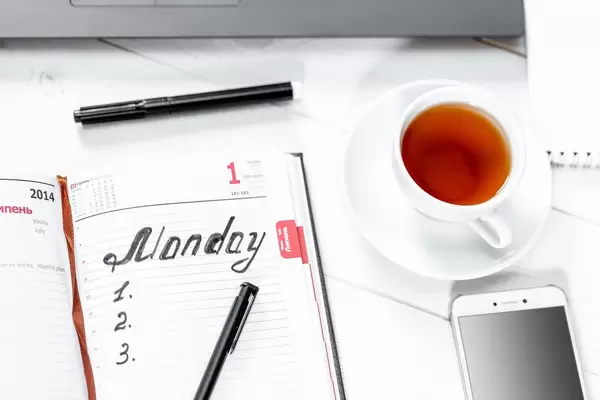 Kalenderbuch mit vorbereiteter To-Do-Liste und Schreiber, einer Tasse Tee und weißem Smartphone