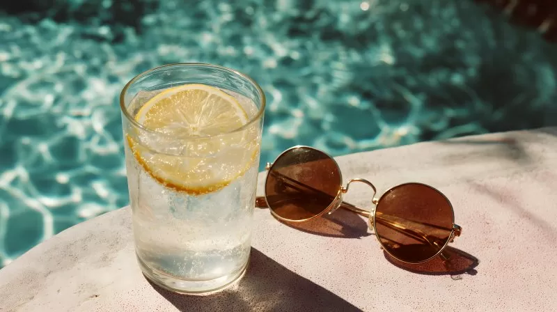 Kaltes Getränk neben Sonnenbrille am Poolrand mit Sonnenschein