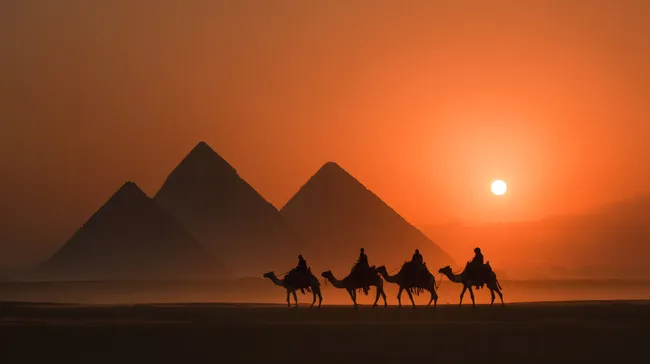 Kamelkarawane vor Pyramiden bei Sonnenuntergang