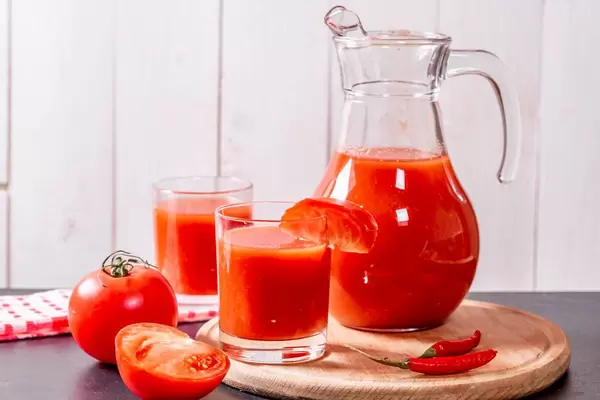 Karaffe und Gläser mit frischem Tomatensaft und Chili auf Holzbrett vor weißer Wand