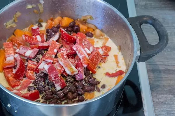 Karibischer Süßkartoffel-Kokos-Eintopf mit schwarzen Bohnen und Paprika im Kochtopf nach Zugabe der Kokosmilch