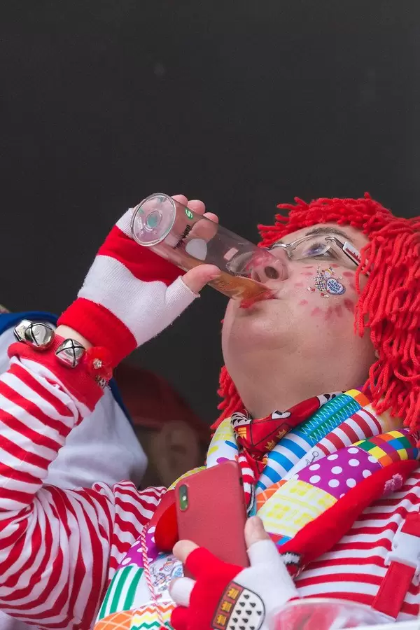 Karneval in Köln: Frau in rot-weißem Kostüm, Handschuhen mit dem Kölner Wappen und roter Perücke trinkt ein Kölsch