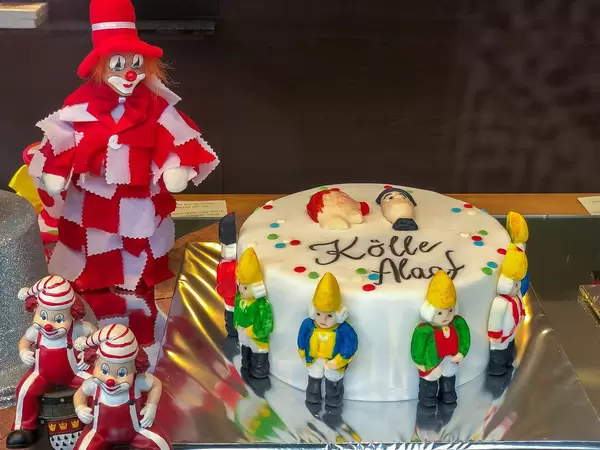 Karneval in Köln: Torte mit dem Narrenruf "Kölle Alaaf" neben Clowns im rot-weiß Kostüm