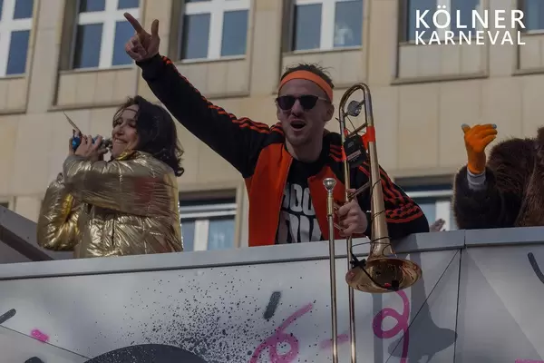 Karnevalist mit Posaune auf einem Festwagen beim Karnevalsumzug, neben dem Bildtitel "Kölner Karneval"