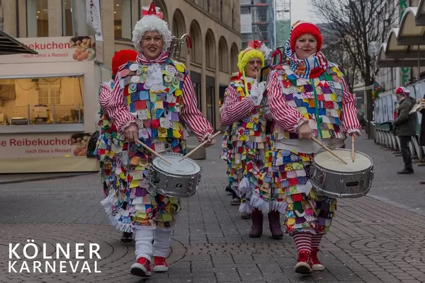 Karnevalisten laufen in Clownskostüm durch die Fußgängerzone und trommeln neben dem Bildtitel "Kölner Karneval"