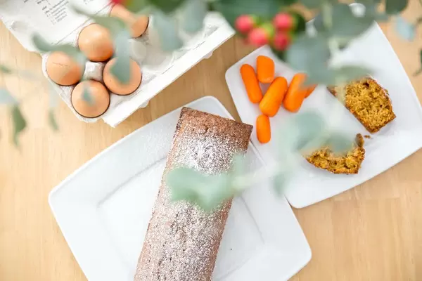 Karottenkuchen, Karotten und Eier mit Blumen im Vordergrund
