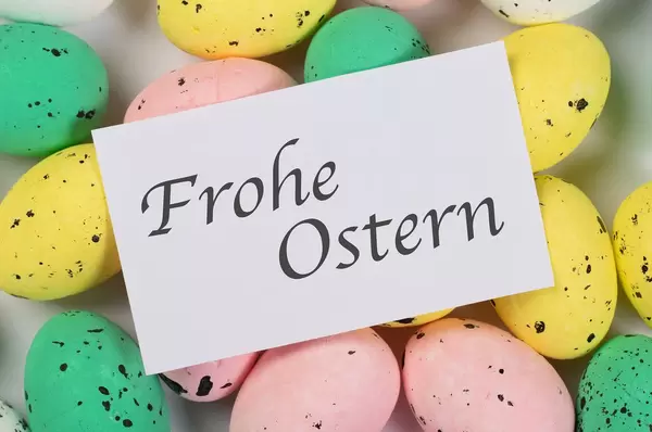 Karte mit Aufschrift FROHE OSTERN liegt auf bunt bemalten Ostereiern