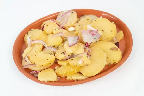 Kartoffelsalat mit geschnittenen Zwiebeln auf einem Teller vor weißem Hintergrund