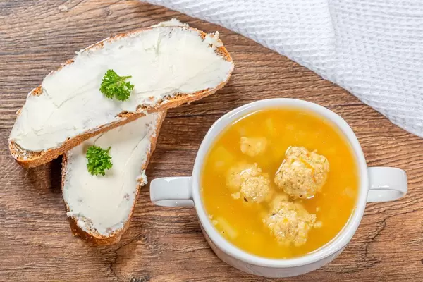 Kartoffelsuppe mit Hühnerfleischbällchen in einer Terrinenform, neben zwei Scheiben Käsebrot