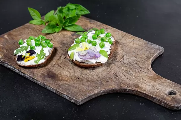 Käsesandwiches mit grünen Erbsen, Basilikumblättern und essbaren Blumen auf einem rustikalen Holzbrett