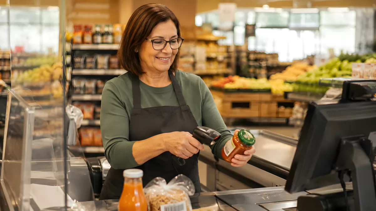 Kassiererin scannt Glas an Supermarktkasse lächelnd