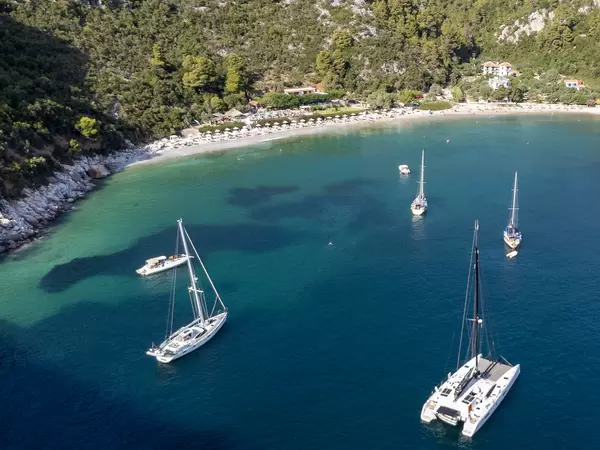 Katamaran und Segelboote in der smaragdgrünen Bucht von Limnonari mit von Kiefern bewachsenen Hügeln