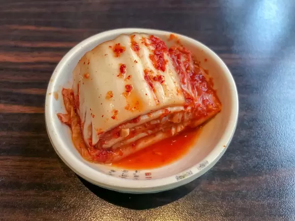 Kimchi, koreanisches Gericht mit Gemüse, hergestellt durch Milchsäuregärung in weiße Teller auf Holztisch