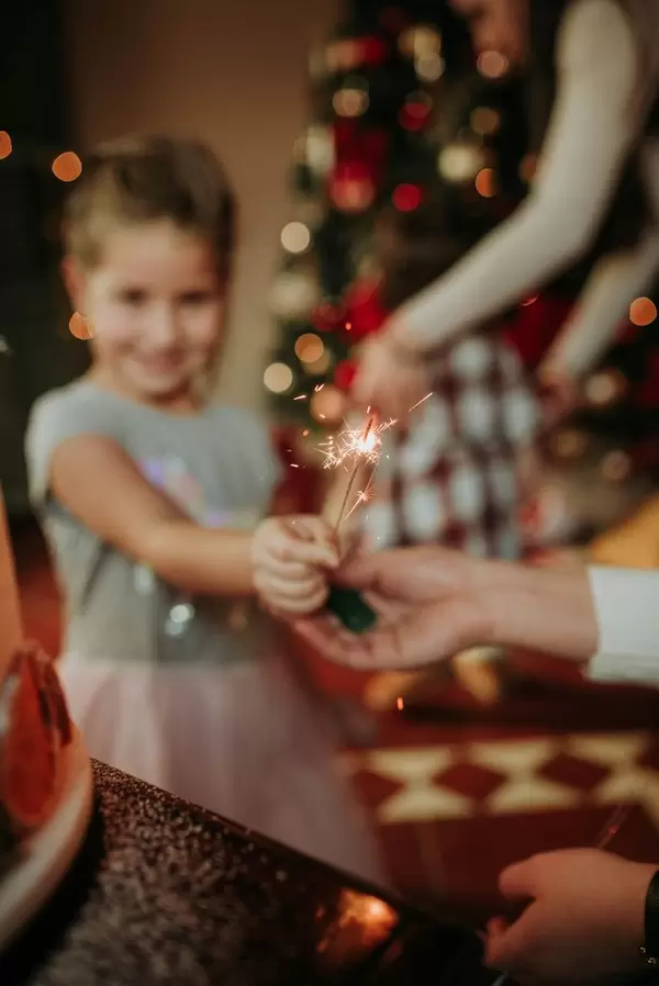 Kind überreicht Wunderkerze vor Tannenbaum und verbreitet festliche Stimmung