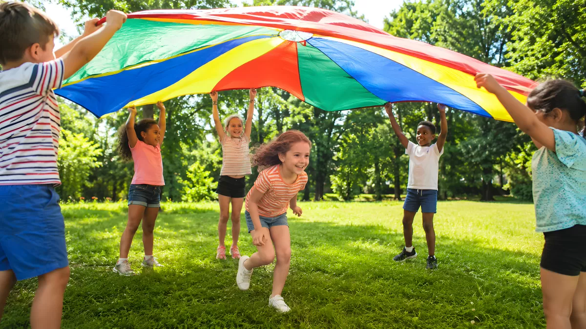 Kinder spielen mit Fallschirm in bunten Farben