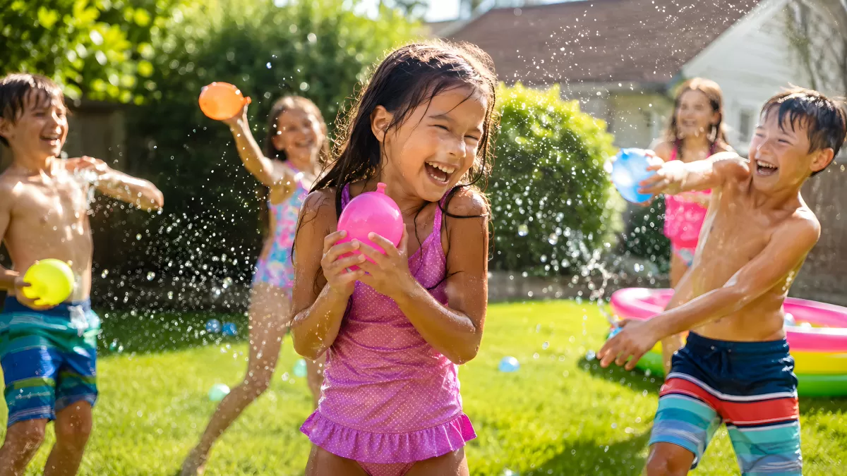 Kinder toben ausgelassen mit Wasserballons im Garten