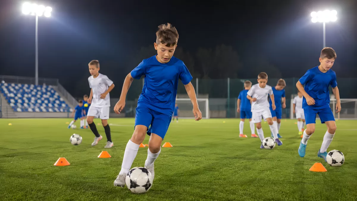 Kinder trainieren Fußball auf beleuchtetem Rasenplatz