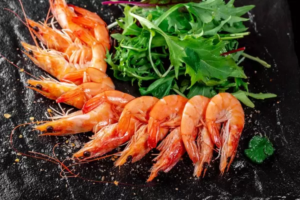 King prawns with fresh arugula leaves on black background