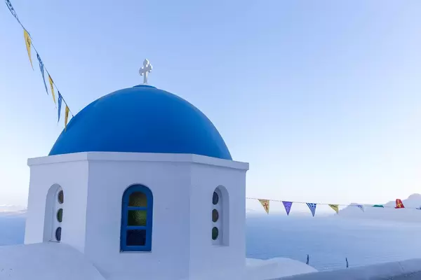 Kirche mit blauer Kuppel und Fahnen auf Santorin mit dem Meer und blauem Himmel