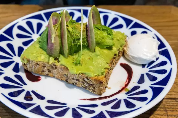 Klassisches Avocado Toast aus Vollkorn mit Avocado, Yuzu & Acai Soße, Pistazien und pochiertem Ei im Flax&Kale Restaurant in Katalonien