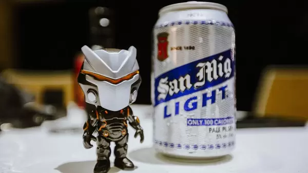 Kleine Actionfigur steht neben silberner Bierdose San Miguel auf weißem Tisch