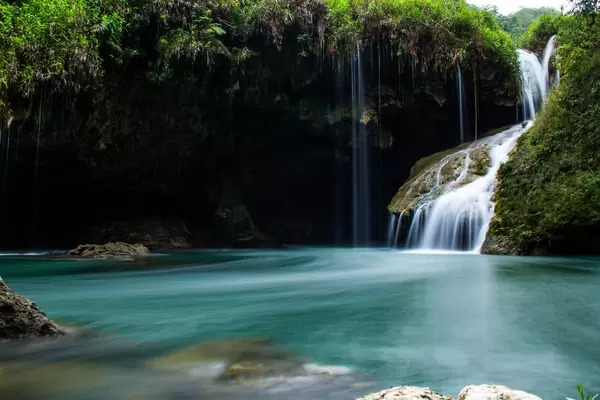 Kleiner Wasserfall führt über mit Moos bewachsenen Felsen in türkisblauen See