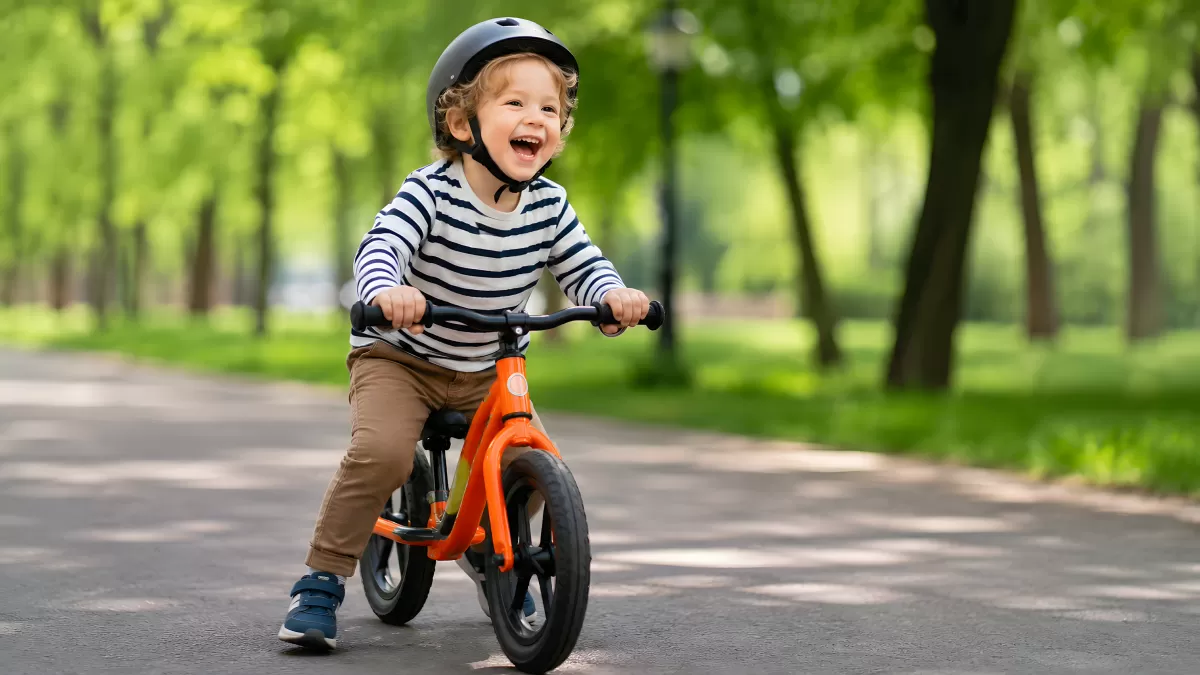 Kleinkind fährt lachend auf orangem Laufrad im Park