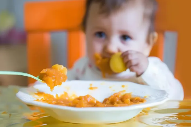Kleinkind isst Brei in bunter Umgebung