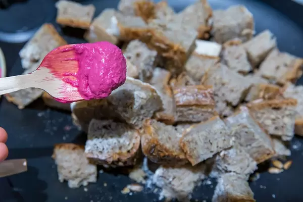 Knalliges Essen: Rote Bete Hummus auf einem Holzlöffel und Brotstücke im Hintergrund