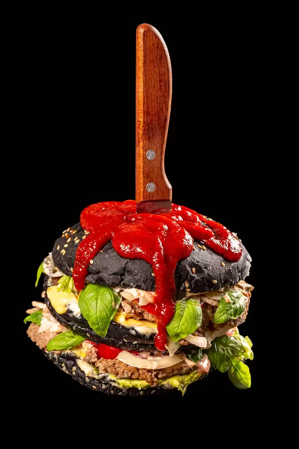 Knife in a black big burger with red sauce on a dark background