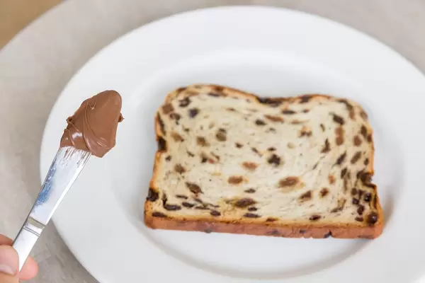 Knife with chocolate spread and fruit bread on white plate