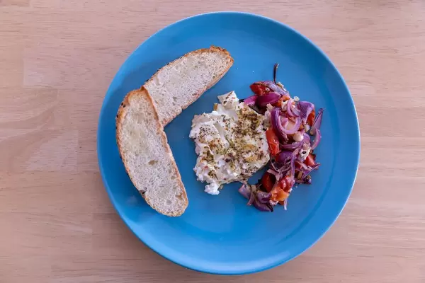 Knoblauch-Fladenbrot und Gebackener Hirtenkäse mit Tomaten-Zwiebel Gemüse auf einem blauen Teller in der Aufsicht
