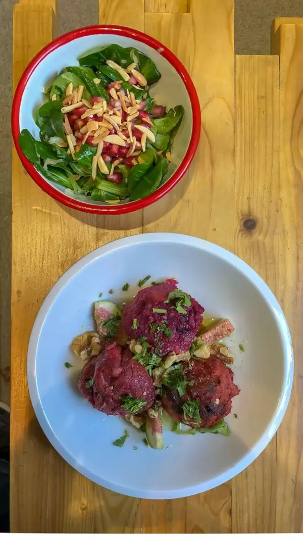 Knödel aus roter Bete mit Koriander, Feigen und Walnüssen und als Beilage Feldsalat mit Sauerkraut, garniert mit Mandeln und Granatapfel auf Holztisch