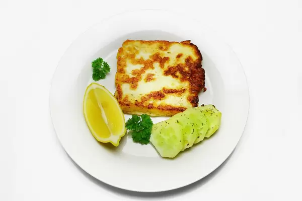 Knusprig braun gebackener Halloumi Käse mit Gurkenscheiben, Zitrone und Petersilie auf Teller