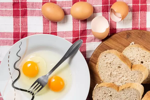 Kochen von French Toast mit Brotscheiben und aufgeschlagenem Ei neben Eiern und Eierschale