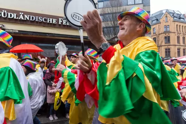 Kölner Jecken in bunten Kostümen trommeln und musizieren während der Straßenparade