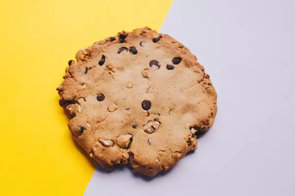 Konzept Food-Fotografie: Selbstgebackener Keks mit Schoko- und Nussstücken auf gelb/lila Untergrund - Nahaufnahme in Draufsicht