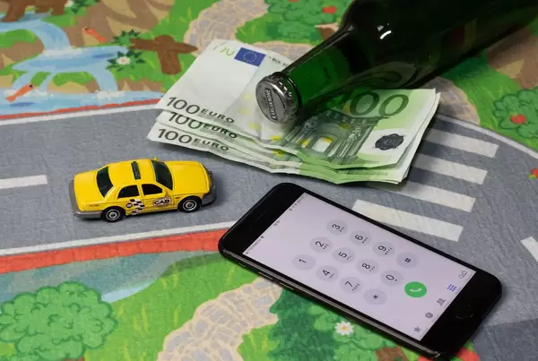 Konzept - Taxidienstleistungen - Ein gelbes Model-Taxi mit Geld, einem Smartphone und einer flasche Bier