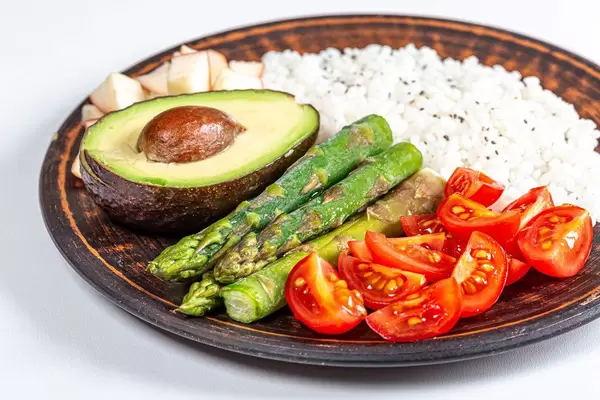 Konzept von gesundem Essen: Tomatenstücke, grüner Spargel, eine halbe Avocado, Äpfelstücke und gekochter Reis