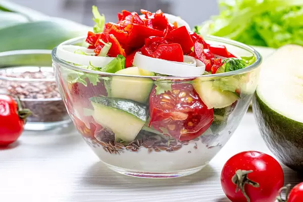 Konzeptbild Diät: frischer Salat mit buntem Gemüse, Leinsamen und Mango, Magermilchjoghurt-Dressing