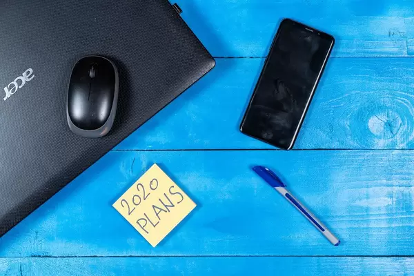 Konzeptbild zum Thema Geschäftsplan für 2020: Notizzettel, Stift, Laptop und Handy auf einem blauen Tisch